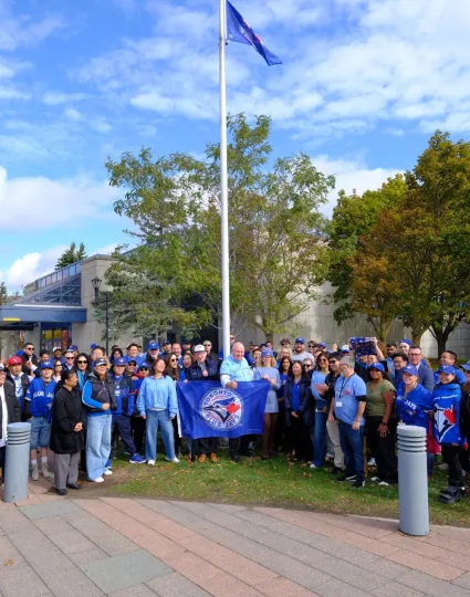 Group of Markham staff wearing blue, holding a Blue Jays flag.